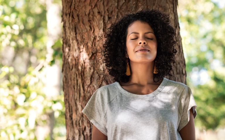 Foto de una mujer pacífica apoyada en un árbol con los ojos cerrados