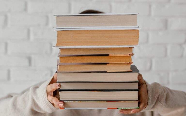 Una guía de lectura consciente: una mujer con un suéter blanco sostiene una pila de libros frente a su cara.